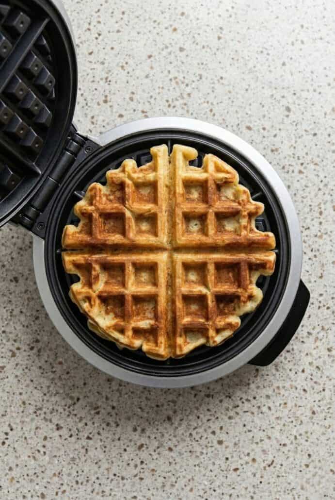 Golden brown potato waffle cooking in a waffle iron, showing how leftover mashed potatoes can be turned into crispy savory waffles.