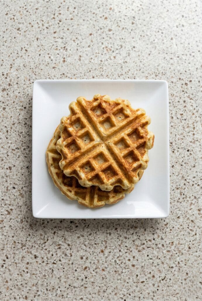 Stack of crispy potato waffles on a white plate, showing a savory waffle.