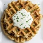 Crispy homemade potato waffle topped with sour cream and chopped chives, a savory waffle made from leftover mashed potatoes.