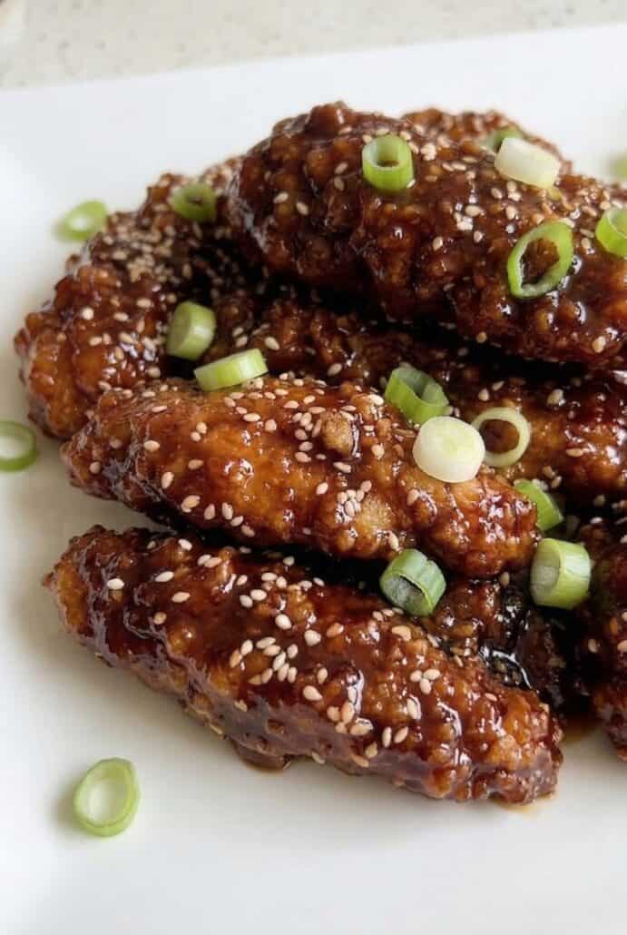 Close-up of crispy Korean fried chicken pieces glazed in a sticky spicy sauce, topped with sesame seeds and green onions for an easy air fryer dish.