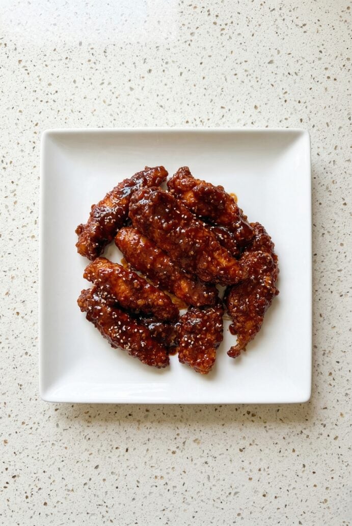 Crispy Korean fried chicken bites coated in a sticky spicy gochujang sauce, served on a white plate.
