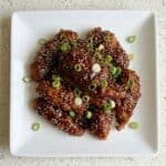 Crispy air fryer Korean fried chicken coated in a glossy spicy sauce and topped with sesame seeds and green onions.