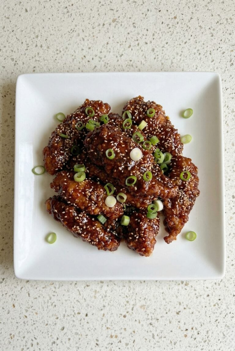 Crispy air fryer Korean fried chicken coated in a glossy spicy sauce and topped with sesame seeds and green onions.