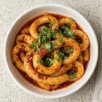 Spicy potato noodles in a bowl garnished with fresh herbs, showcasing the chewy texture and chili oil sauce.