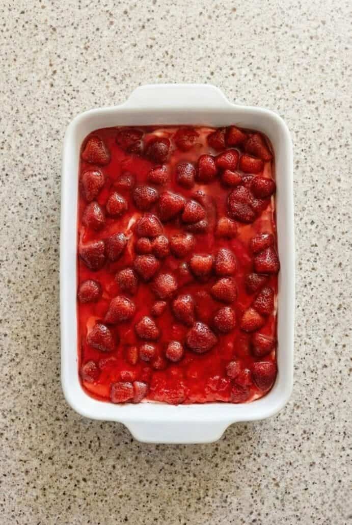 Top view of strawberry pretzel salad in a baking dish, showing the glossy strawberry Jell-O and whole strawberries layered over the creamy filling in this classic sweet and salty dessert recipe.