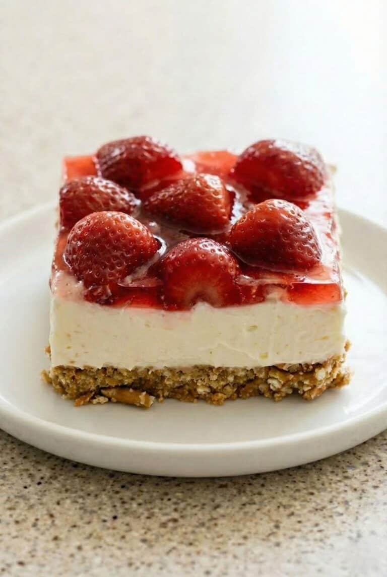 Slice of strawberry pretzel salad with creamy cheesecake layer, fresh strawberry topping, and buttery pretzel crust.