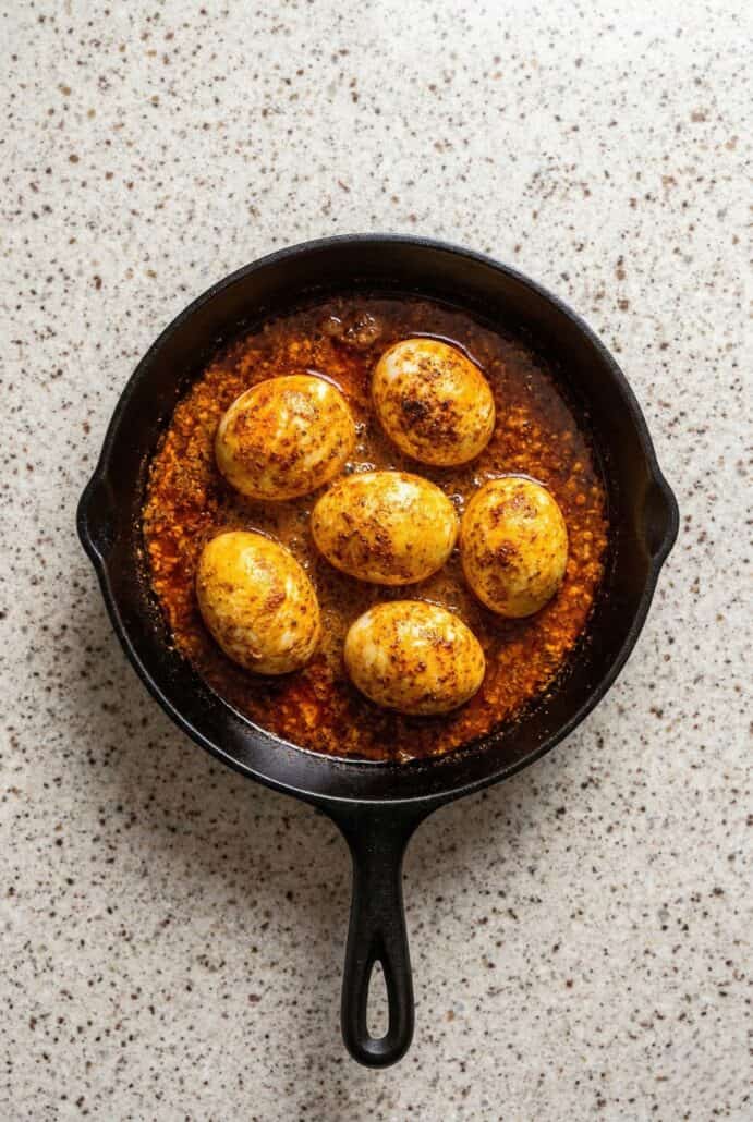 TikTok egg boil in a skillet with spicy butter sauce, showing boiled eggs coated in Cajun seasoning.
