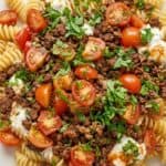 Plate of fusilli pasta topped with ground beef, cherry tomatoes, and fresh parsley.