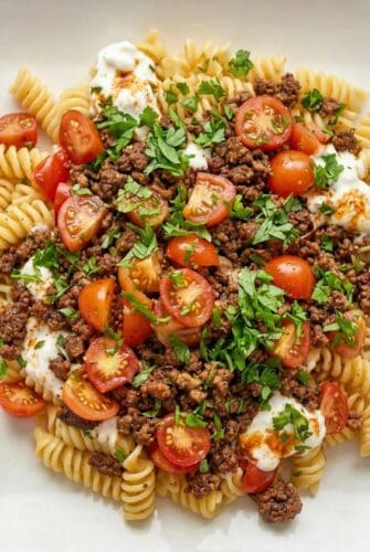 Easy Turkish Pasta Recipe With Ground Beef And Yogurt Sauce Plate of fusilli pasta topped with ground beef, cherry tomatoes, and fresh parsley.