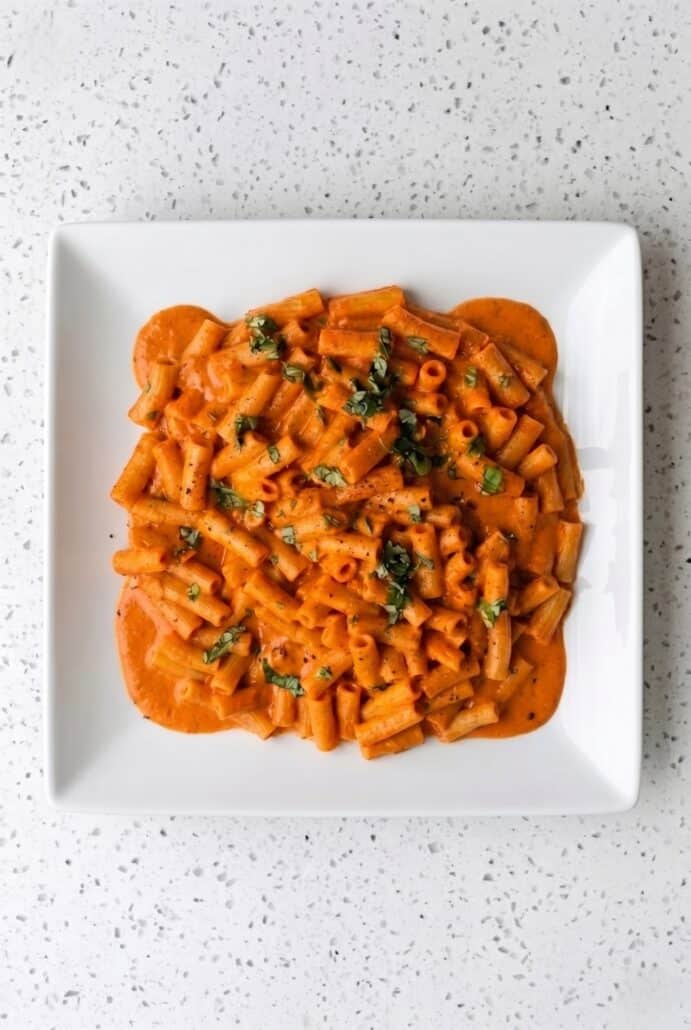 Plated creamy red pepper pasta topped with fresh basil, featured in this quick and easy weeknight dinner recipe.