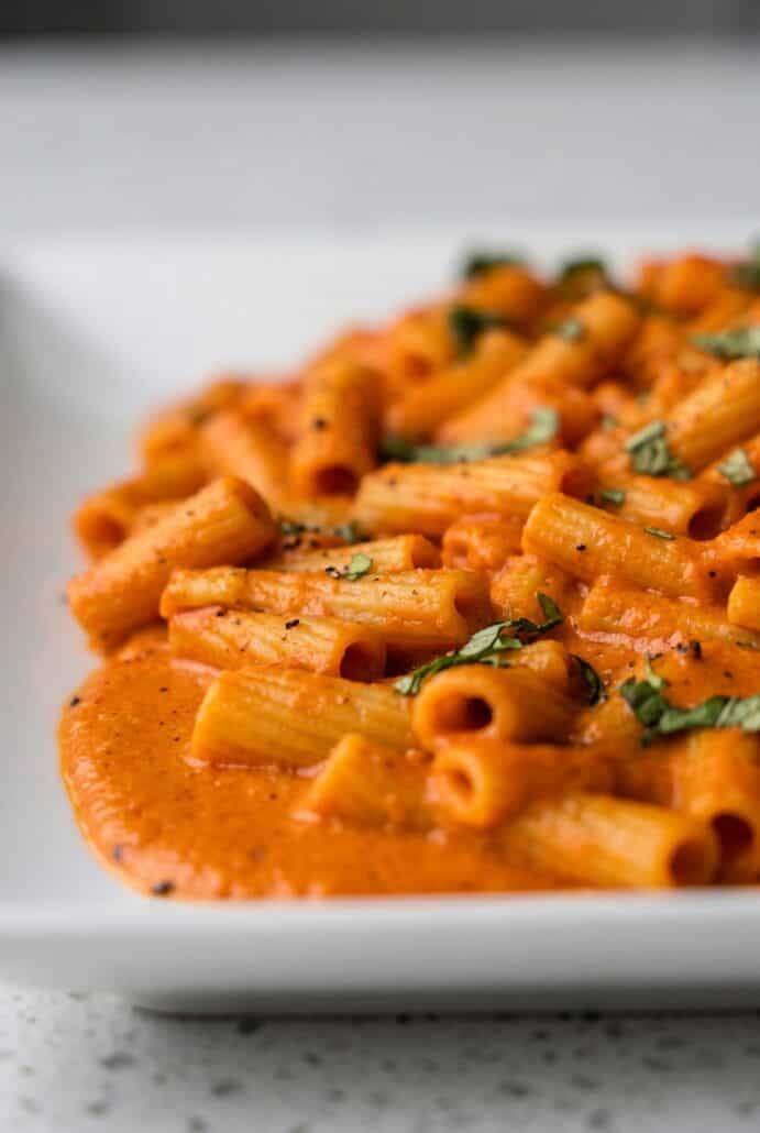 Close-up of creamy red pepper pasta with rigatoni and fresh basil.