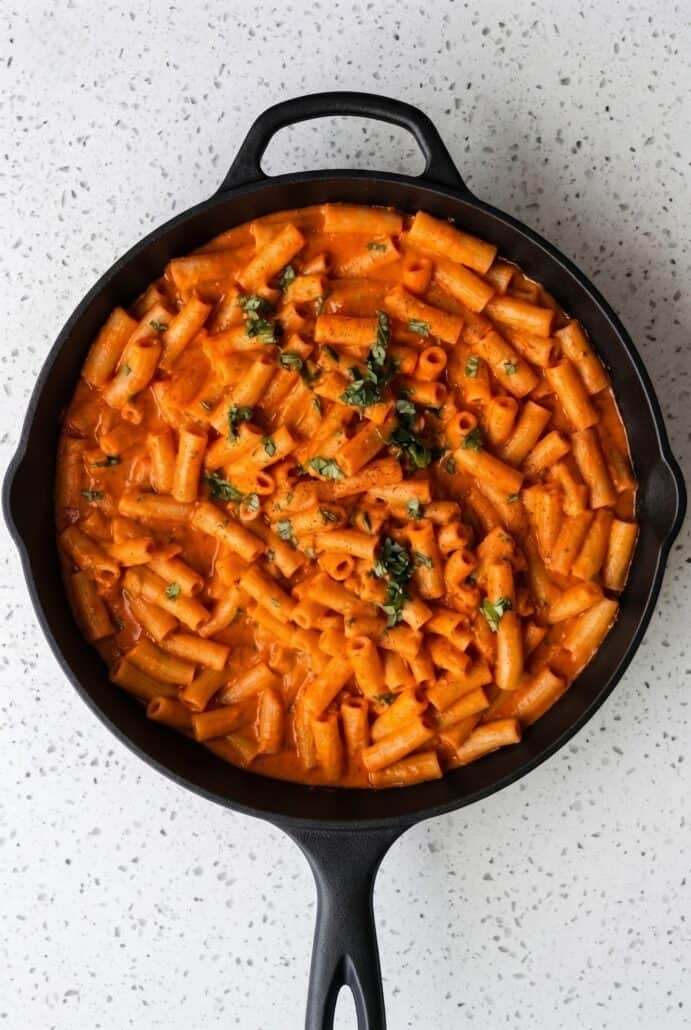 Skillet of creamy red pepper pasta topped with fresh basil, shown in this easy one-pan weeknight dinner recipe.