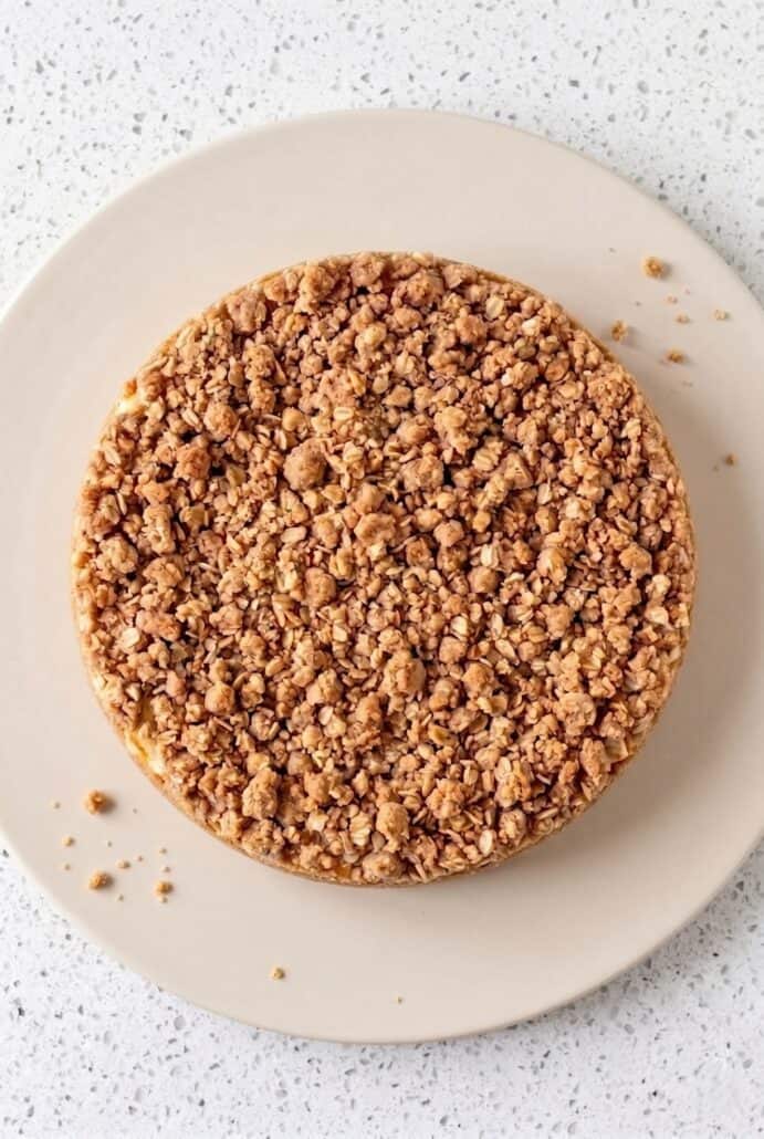 A top view of a golden-brown apple crisp cheesecake with a crunchy oatmeal crumble topping.