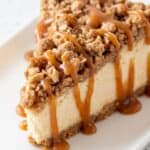 A slice of apple crisp cheesecake topped with a crunchy oatmeal crumble and drizzled with caramel sauce.