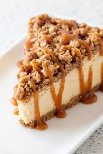 Apple Crisp Cheesecake – The Ultimate Fall Dessert Recipe A slice of apple crisp cheesecake topped with a crunchy oatmeal crumble and drizzled with caramel sauce.