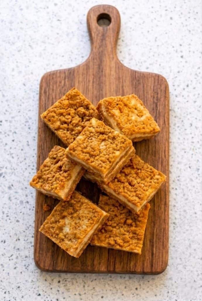 Stack of butterscotch graham cracker cheesecake bars on a wooden board, showing chewy layers and crumb topping.