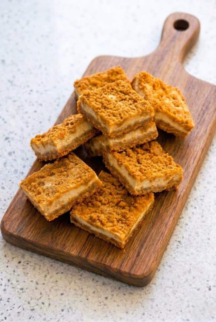 Stacked butterscotch graham cracker cheesecake bars on a wooden board, highlighting the chewy crust and creamy cheesecake layers.