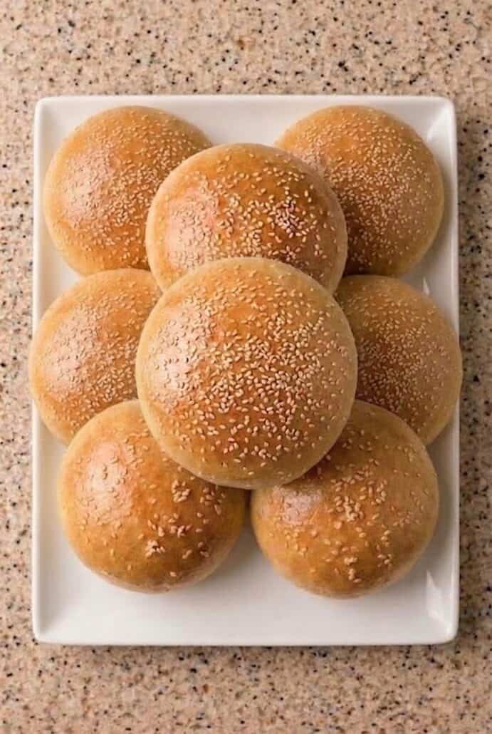 Plate of golden brown sesame hamburger buns stacked together.