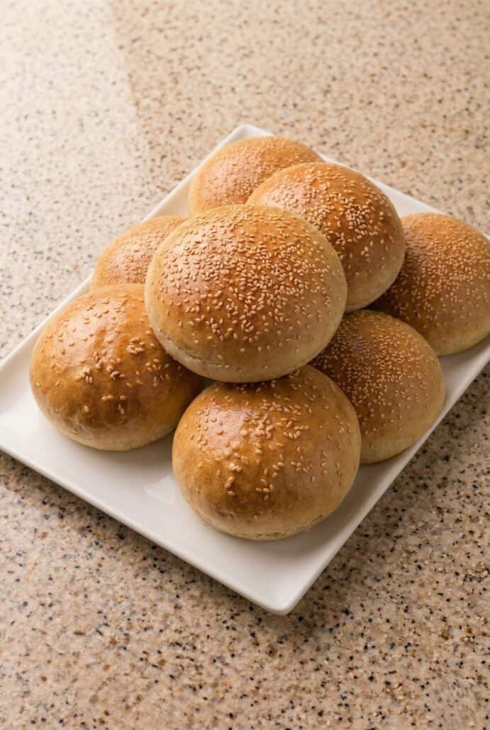 Golden homemade hamburger buns with sesame seeds served on a plate for easy burger buns recipe.