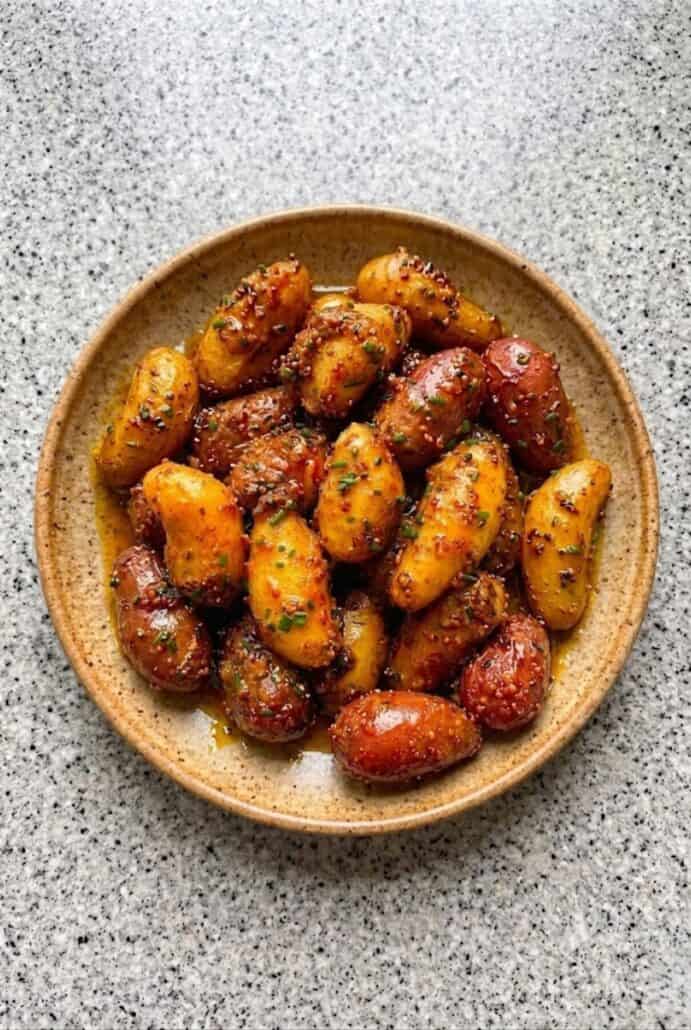 Close-up of honey mustard roasted baby potatoes in a bowl, showcasing a glossy glaze and herbs.