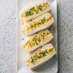 Japanese egg sandwiches arranged on a platter with creamy tamago filling and soft crustless bread.