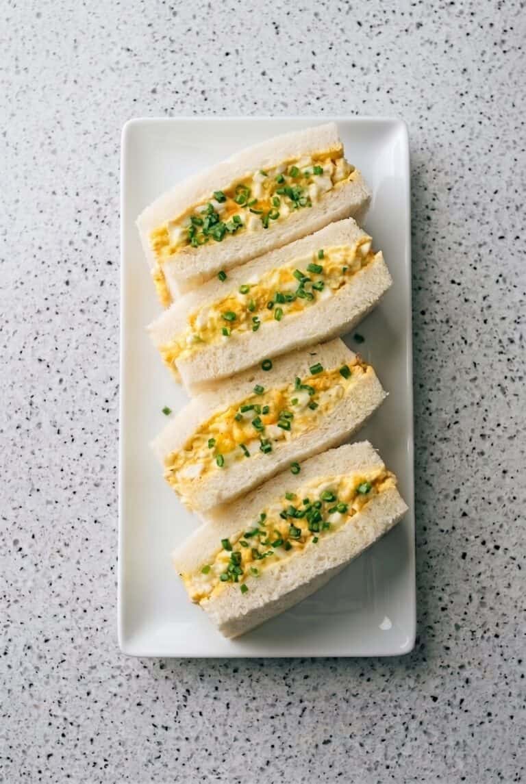 Japanese egg sandwiches arranged on a platter with creamy tamago filling and soft crustless bread.