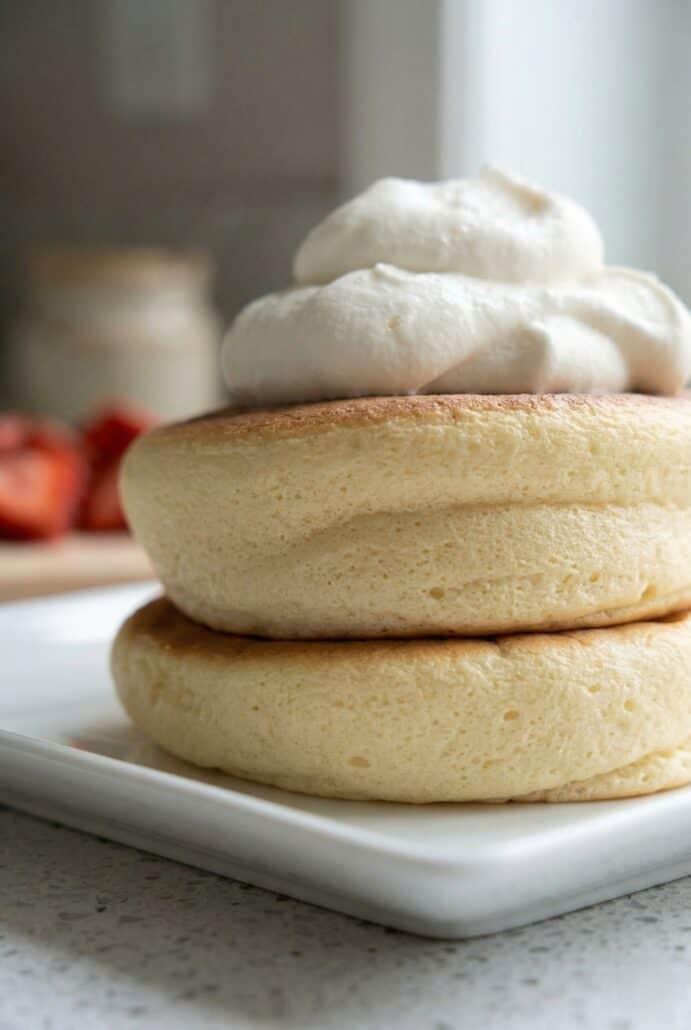 Close-up of thick and fluffy Japanese soufflé pancakes with whipped cream, showcasing their soft, airy texture.