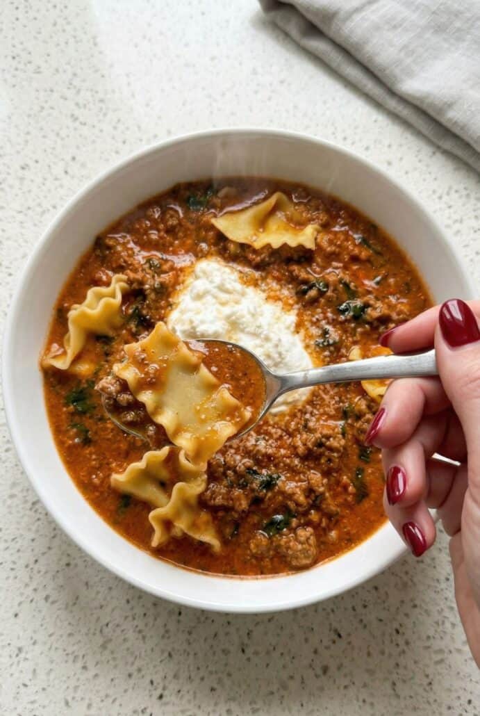 Hand holding a spoon scooping cheesy lasagna soup with pasta and ricotta, showing the creamy texture of this easy one-pot meal.