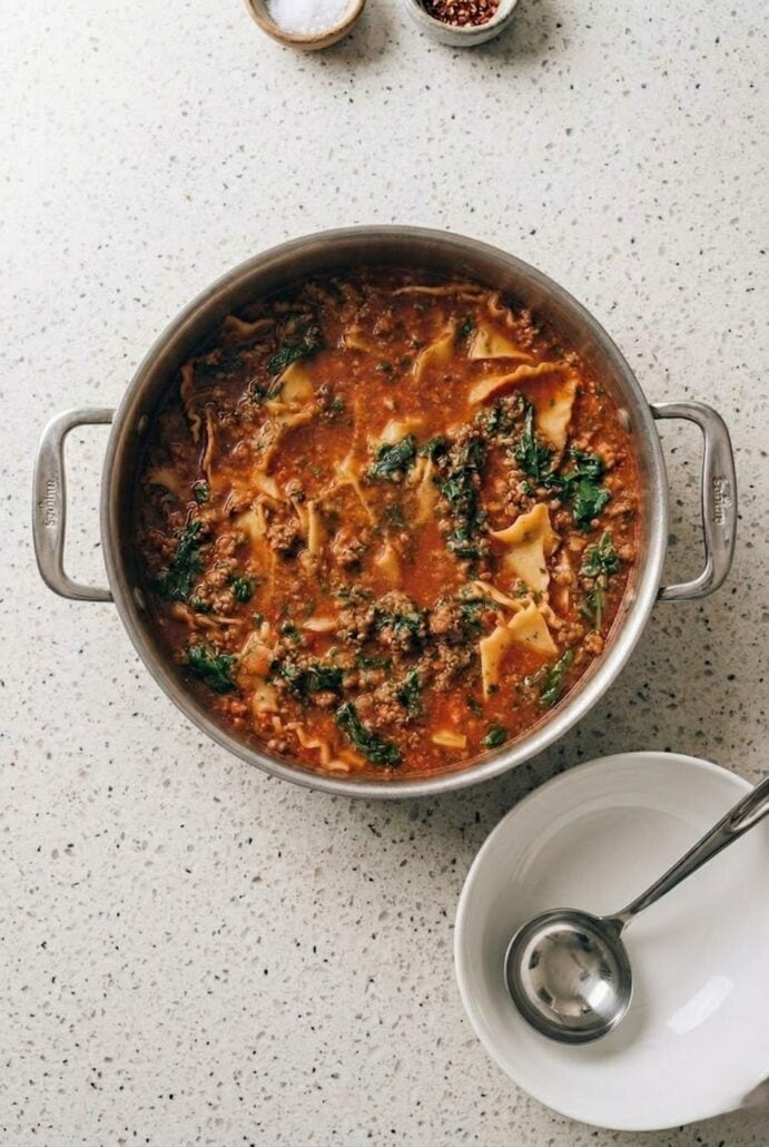 Lasagna soup cooking in a pot with ground beef, spinach, and pasta in rich tomato broth.