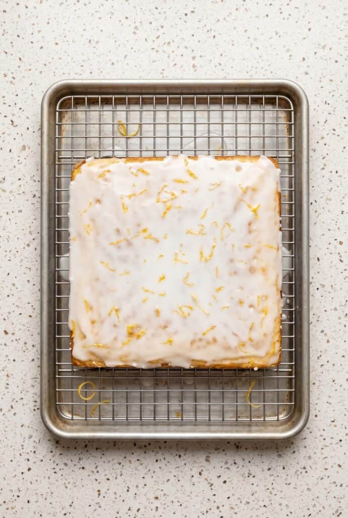 Lemon brownies cooling on a rack with glossy lemon glaze and zest, showing the finished texture before slicing for this easy citrus dessert recipe.