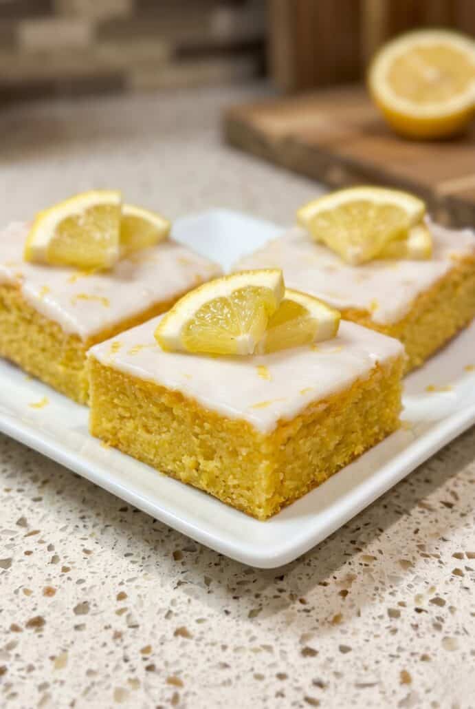Lemon brownies with glaze and fresh lemon slices on top, served as a bright citrus dessert.