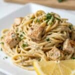 Creamy lemon chicken pasta with spaghetti, tender chicken, and a rich garlic Parmesan sauce served with fresh lemon wedges.