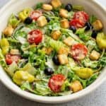 Fresh Olive Garden-style salad with lettuce, chickpeas, tomatoes, olives, and zesty dressing in a bowl.
