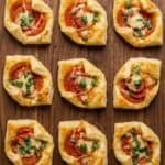 Air fryer pepperoni basil tomato puff pastry bites served on a wooden board.