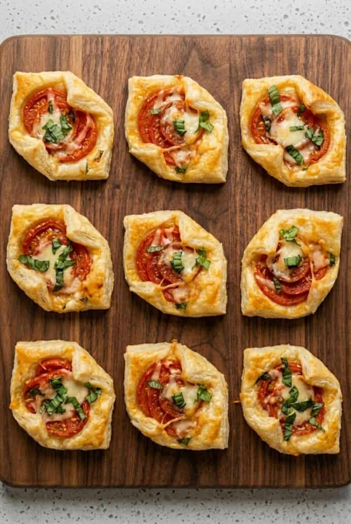 Air fryer pepperoni basil tomato puff pastry bites served on a wooden board.