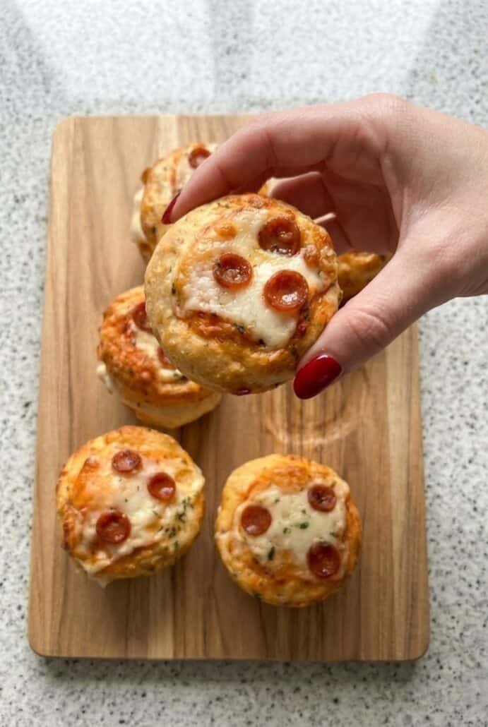 A hand holding one mini pizza cupcake with melted cheese and pepperoni.