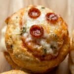 Close-up of a single mini pizza cupcake with melted cheese, pepperoni, and a sprinkle of herbs, showing its golden, crispy texture.