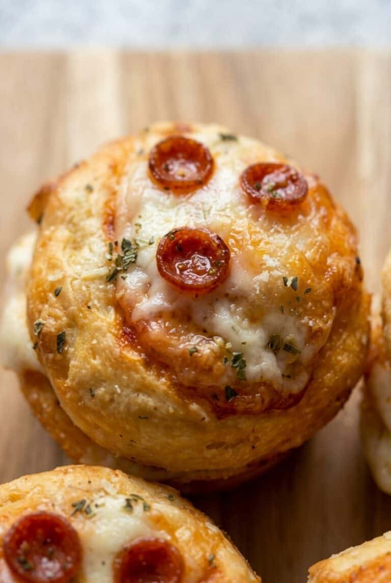 Close-up of a single mini pizza cupcake with melted cheese, pepperoni, and a sprinkle of herbs, showing its golden, crispy texture.