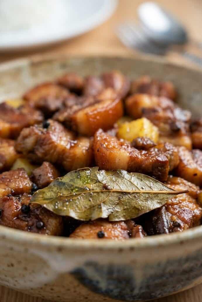 Close-up of Pork Hamonado with tender pork belly, pineapple chunks, and bay leaf in a rich sweet savory sauce.