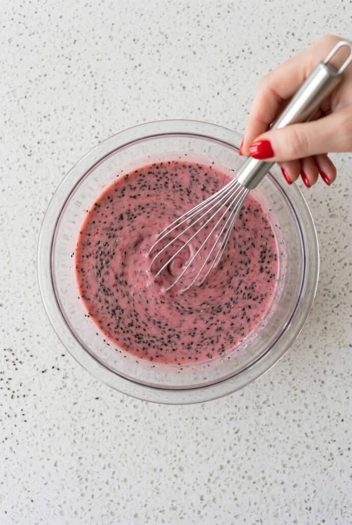Chia seeds being whisked into raspberry mixture, showing how to combine ingredients.
