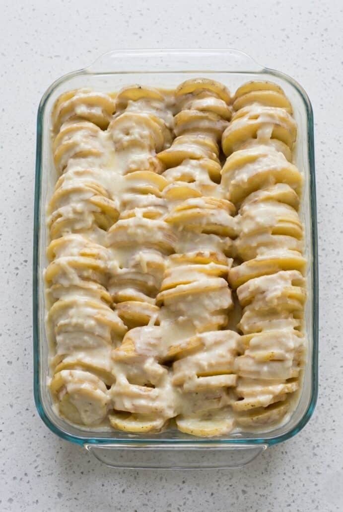 Unbaked scalloped potatoes layered in a casserole dish, showing the creamy sauce before baking.