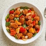 Bowl of homemade sweet and sour pork with crispy pork pieces, pineapple, and colorful vegetables.