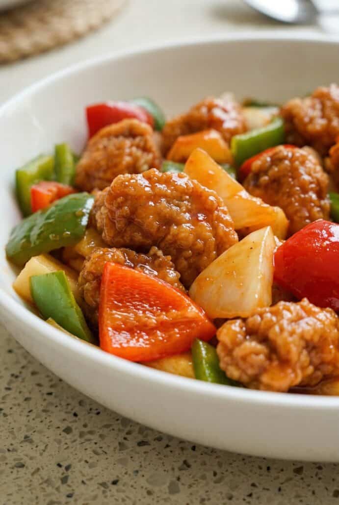 Crispy sweet and sour pork with pineapple, bell peppers, and snap peas served in a bowl.