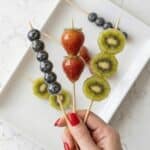 Tanghulu fruit skewers with strawberries, kiwi, and blueberries coated in glossy sugar syrup.