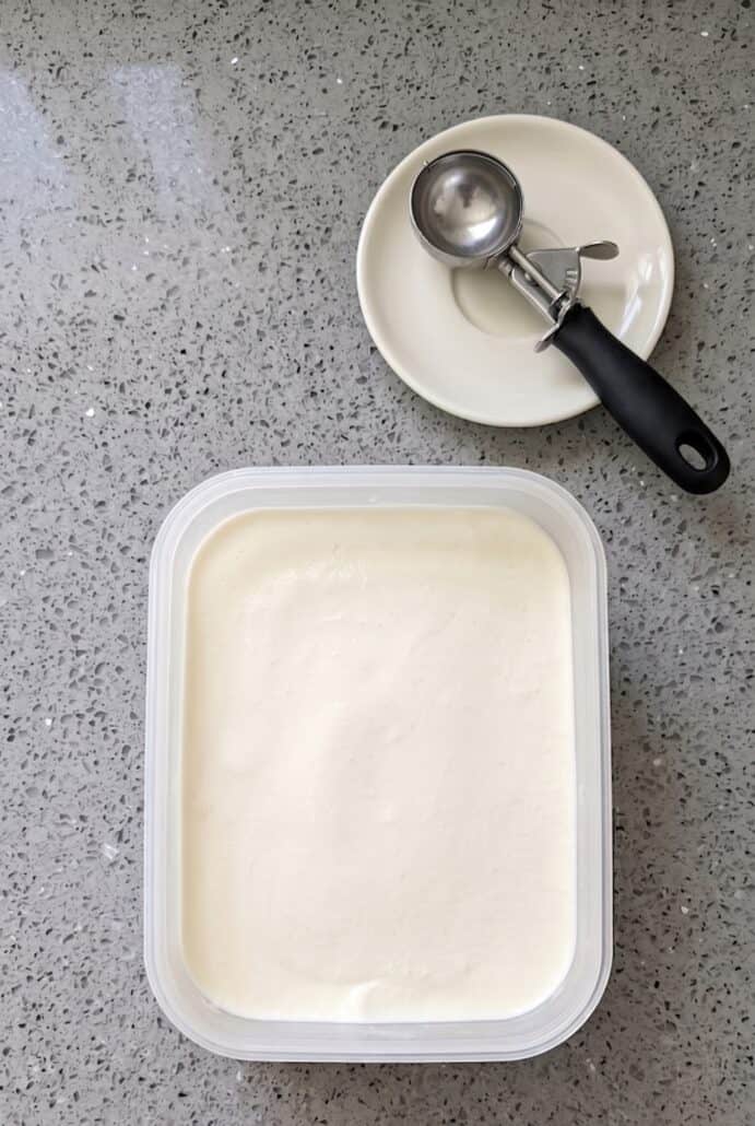 Finished no-churn vanilla ice cream in a container with scoop, ready to serve.