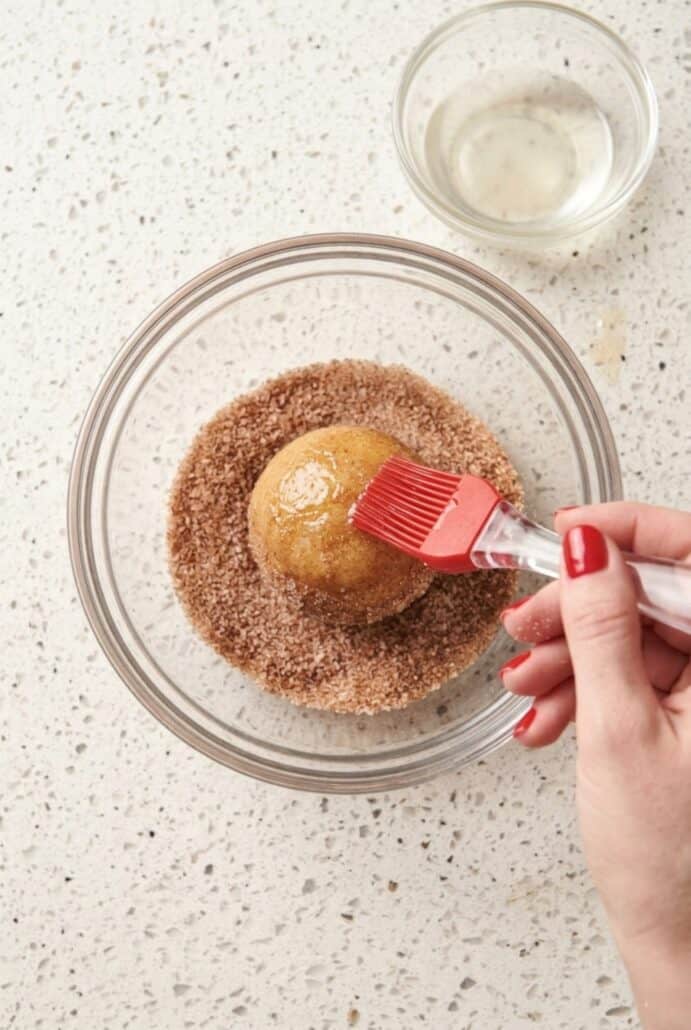 Cinnamon sugar mixture being brushed onto warm air fryer banana donut holes.