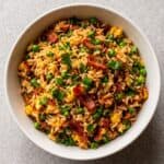 Bowl of bacon fried rice with eggs, peas, carrots, and green onions.