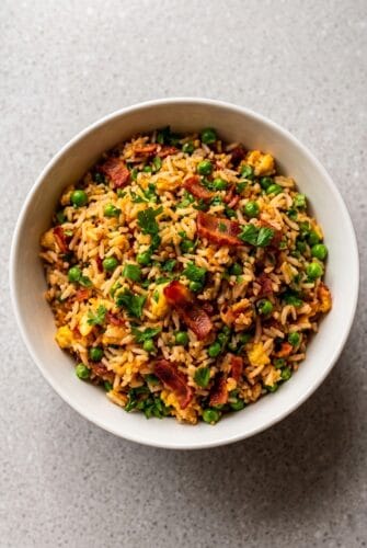Easy Bacon Fried Rice Recipe - Better Than Takeout! Bowl of bacon fried rice with eggs, peas, carrots, and green onions.