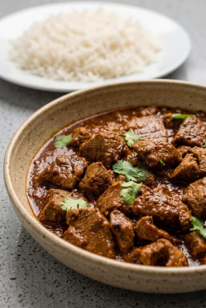 Close-up of tender beef vindaloo in rich curry sauce, with basmati rice in the background.