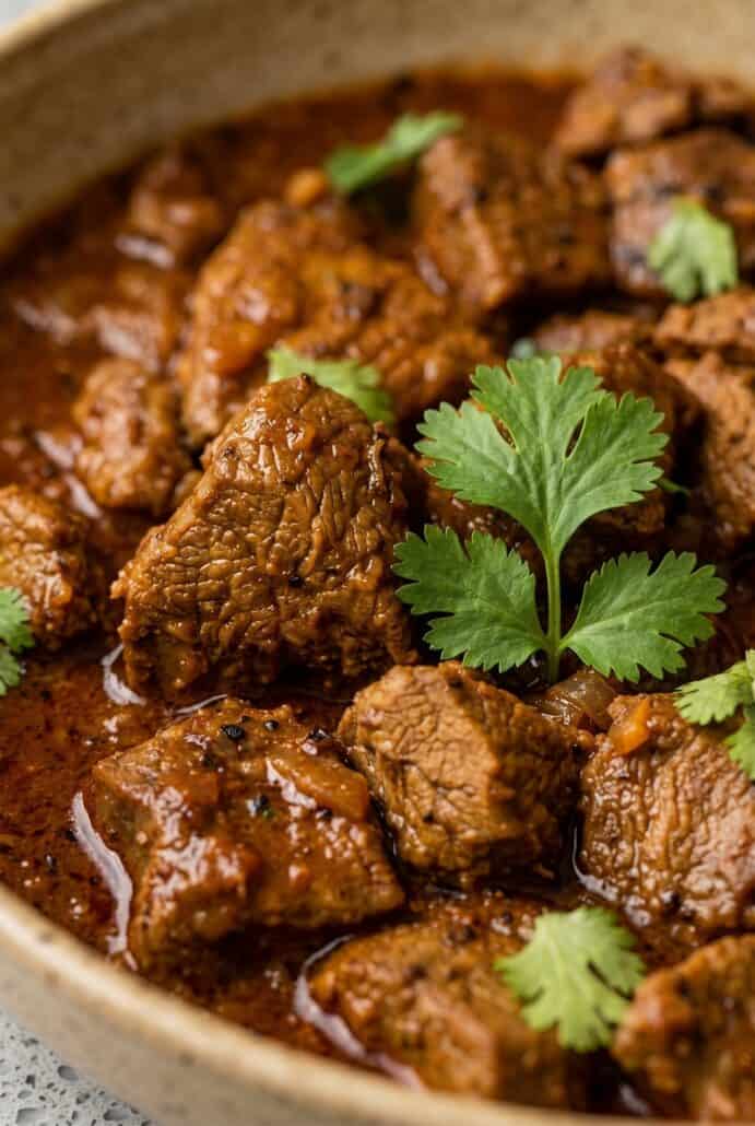 Close-up of tender beef vindaloo curry garnished with fresh cilantro.